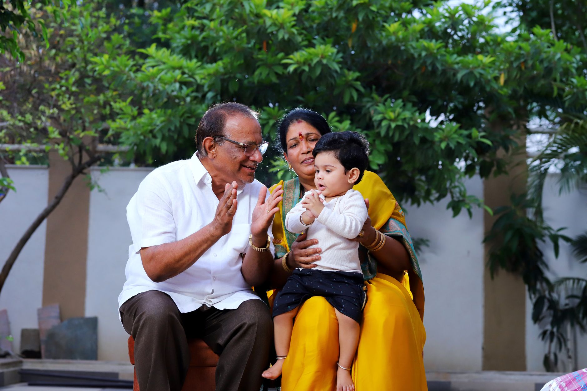 Indian grandparents lovingly holding and playing with a toddler outdoors in a home garden