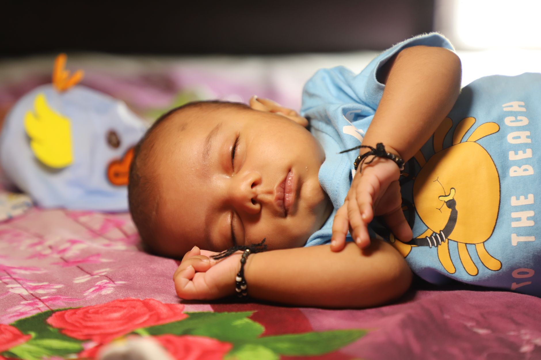 An Indian toddler asleep on a colorful floral bedspread during afternoon nap time