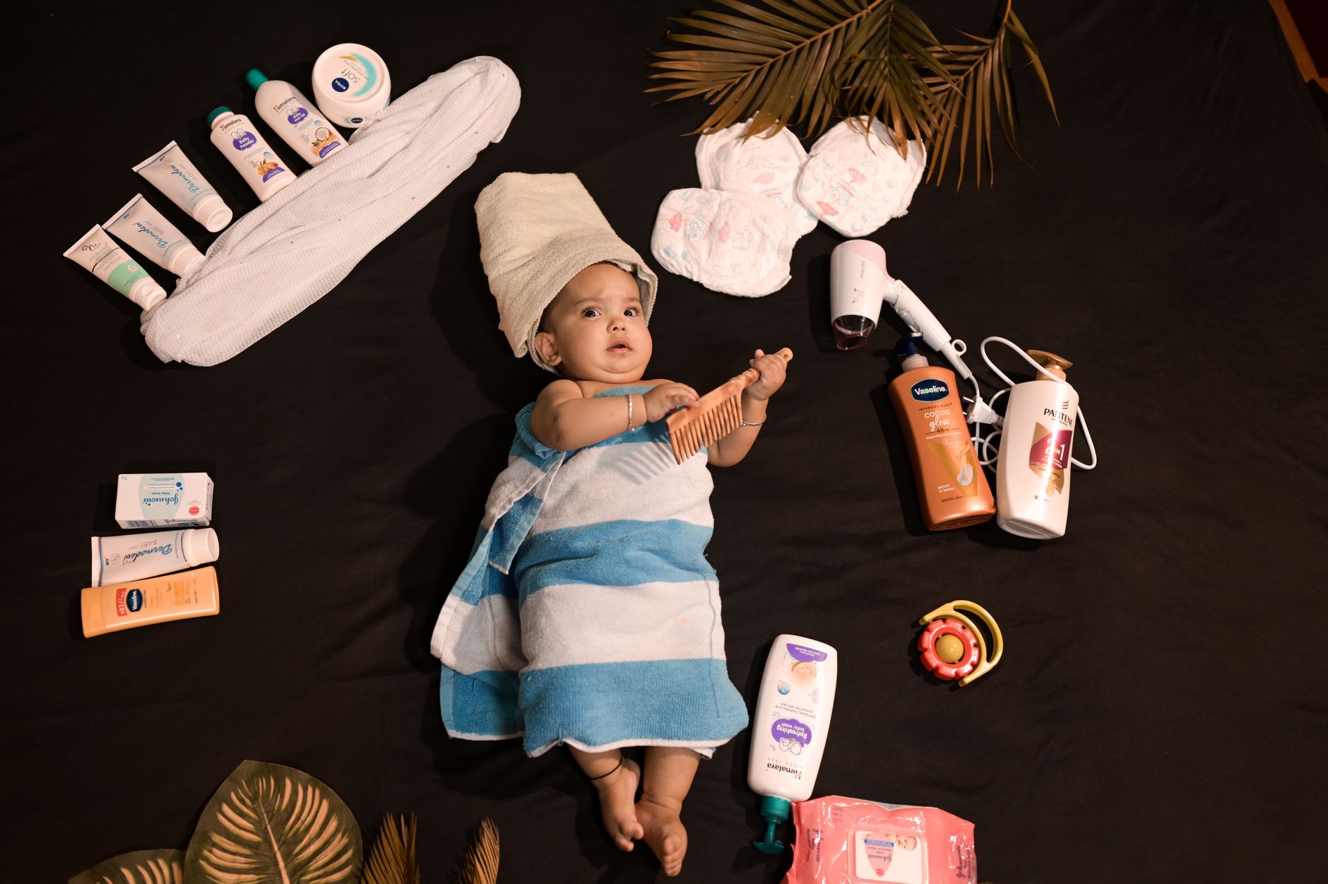 An Indian baby wrapped in a towel after a bath, surrounded by baby lotions, creams, and skincare essentials