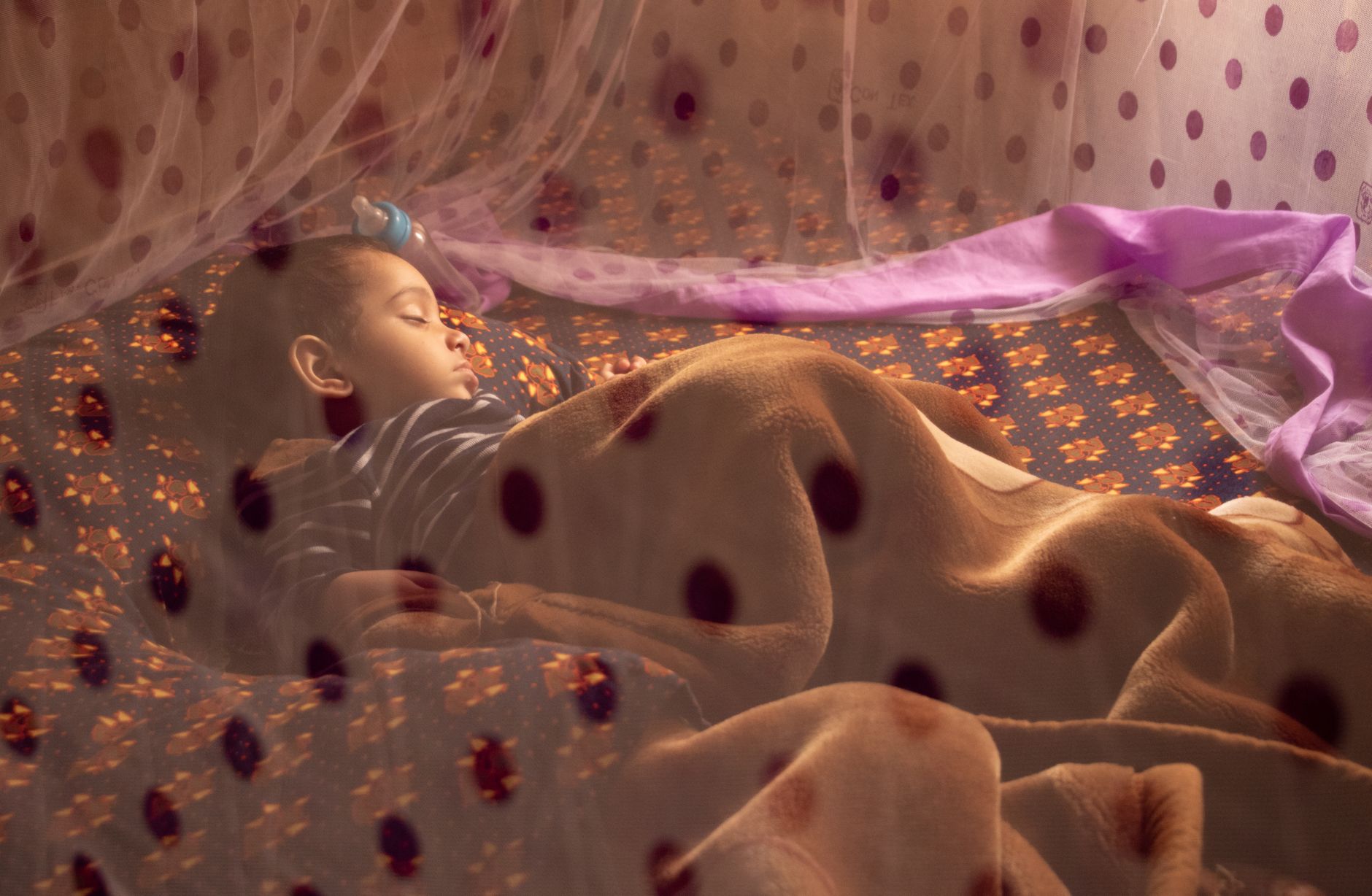 A baby sleeping peacefully under a mosquito net, tucked into a bed with soft blankets