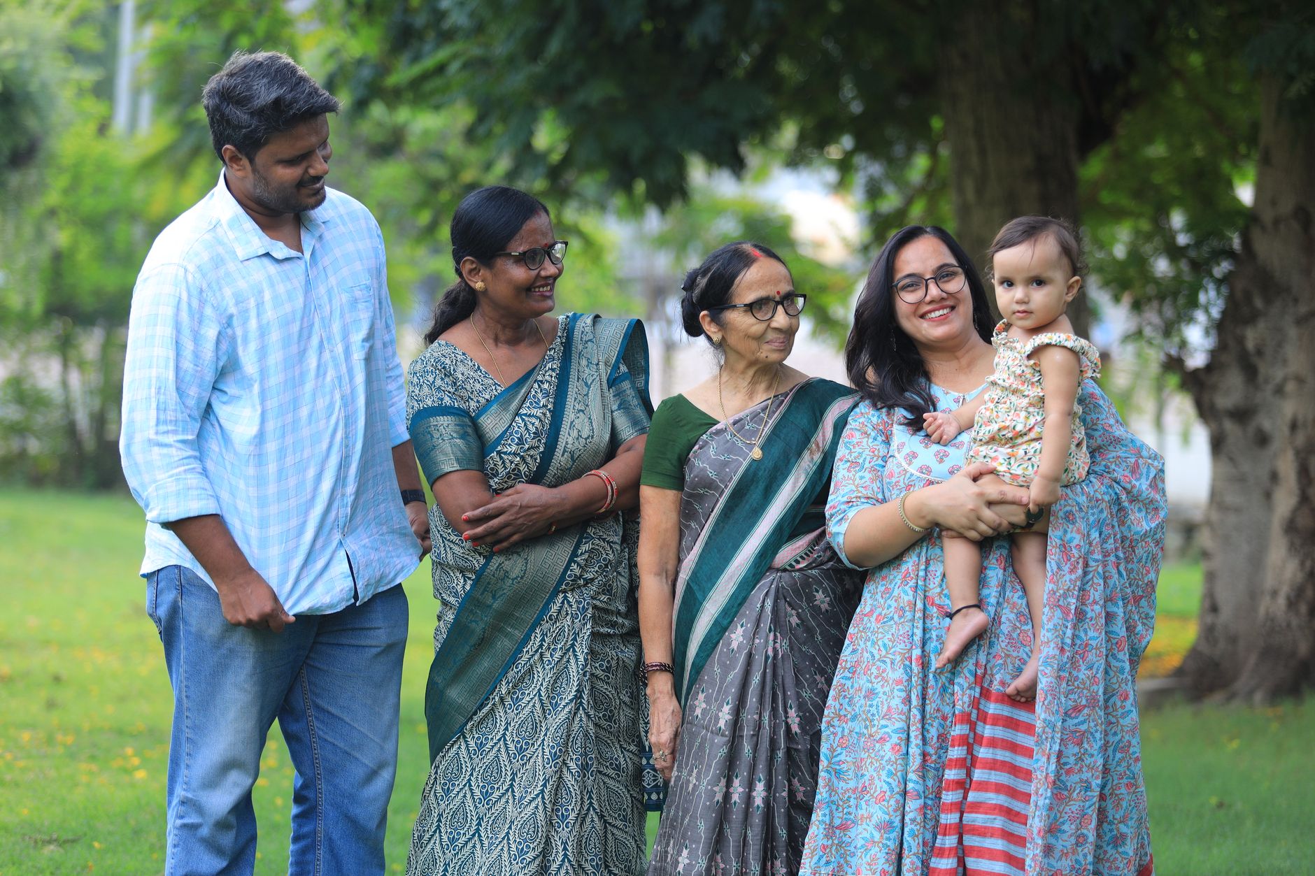 Three generations of an Indian family — grandmother, mother, and baby, with father alongside — standing together outdoors