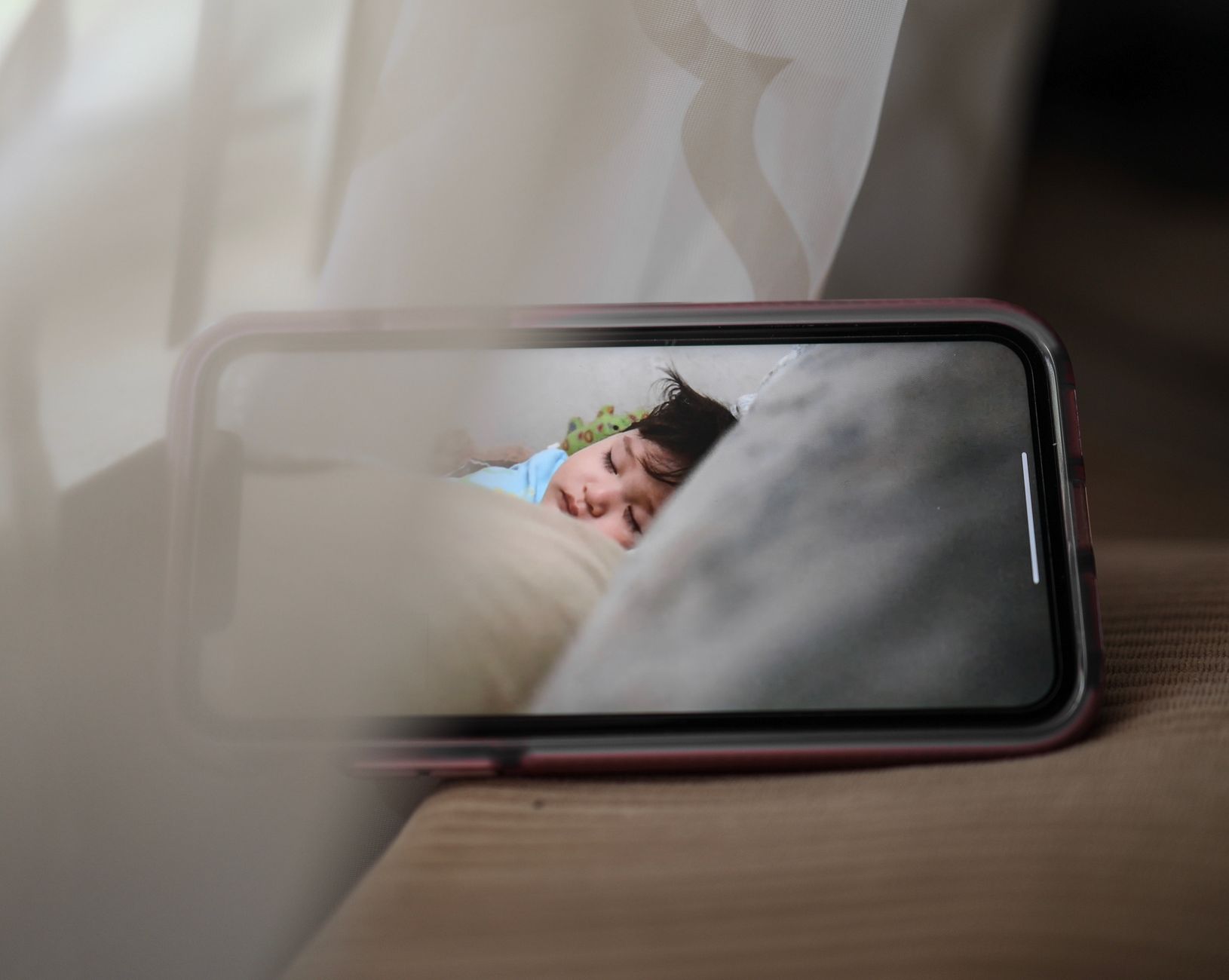 A smartphone propped on a table showing a live baby monitor feed of a baby sleeping in a crib