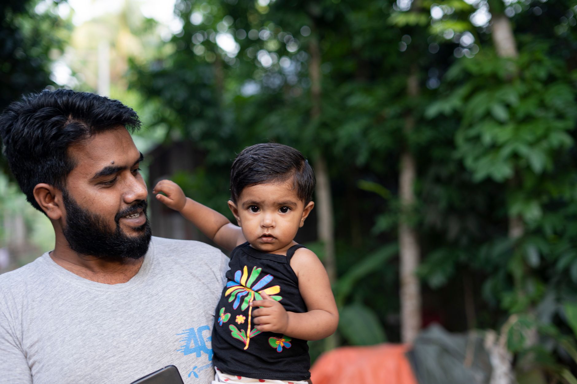 An Indian father sits close outdoors with his baby daughter, holding her hands during a quiet bonding moment